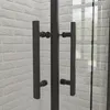 A close-up view of black shower door handles against a white brick wall. Produktbild-Vorschau