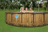Three people are in a round wooden-look above-ground pool in a grassy backyard. Produktbild-Vorschau