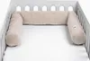 A beige, U-shaped crib bumper, also known as a bed snake, is placed inside a white crib. Produktbild-Vorschau