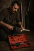 A man is kneeling and using a pipe welding tool to join two white plastic pipes. A red toolbox containing the tool and accessories is open on the floor. Anteprima dell’immagine prodotto