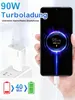A hand holding a smartphone displaying a charging animation, next to a white USB-C charger plugged into a wall socket. Produktbild-Vorschau