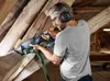 A man is using a reciprocating saw to cut through wooden beams in an attic. Voir les images du produit
