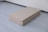 A folded beige gymnastics mat is shown on a light gray wooden floor against a white wall. Náhled obrázku produktu