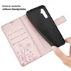 A hand is holding a black phone case, which is being placed into a rose gold flip case with card slots and a floral design. Produktbild-Vorschau