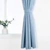 A light blue curtain is tied back with a fabric band, hanging next to a window with a vase of greenery on the sill. Produktbild-Vorschau
