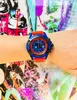 A person's wrist wearing a watch, with a colorful, graffiti-style background. Náhled obrázku produktu