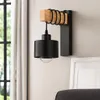 A black hanging wall lamp with a wooden accent is mounted on a light-colored wall, with a window and curtains visible in the background. Náhľad obrázku produktu