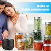 A couple is in a kitchen preparing food, with several mason jars filled with various preserved foods and vegetables displayed in the foreground. A black vacuum sealer device is also visible. Produktbild-Vorschau