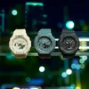 Three Casio G-Shock watches are displayed on a shelf with a blurred city background. Produktbild-Vorschau