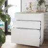 A white dresser with three drawers is shown in a room with a large window and a plant. Voir les images du produit