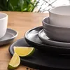 A close-up shot of stacked ceramic dishes and bowls on a wooden table, with lime slices in the foreground. Náhled obrázku produktu