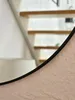 A close-up view of a round mirror with a black frame, reflecting a staircase with wooden shelves. Produktbild-Vorschau