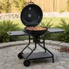 A black charcoal grill with food cooking on it, set up on a stone patio in a backyard. Produktbild-Vorschau