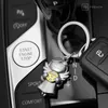 A close-up shot of a car's interior, focusing on the start/stop button and a keychain with an angel charm. Produktbild-Vorschau
