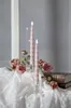 Two pink LED candles in glass holders are placed on a white lace tablecloth, surrounded by pink roses and two old books. Produktbild-Vorschau