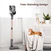 A cordless vacuum cleaner stands next to a sofa where an orange cat is lounging. Produktbild-Vorschau