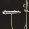 A close-up view of a chrome thermostatic shower mixer and hose against a black marble background. Produktbild-Vorschau