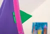 A close-up of a purple hanging chair with pink trim, showing two green tags. A small green triangle is visible. Náhled obrázku produktu
