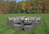 A wicker lounge set with cushions and a glass-topped table is placed on a grassy lawn in front of a wooded area with autumn foliage. Produktbild-Vorschau