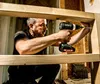 A man is using a cordless drill to screw into a wooden frame. Produktbild-Vorschau