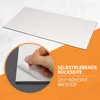 A close-up of a hand peeling the backing off a self-adhesive surface, with a larger image of the product in the background. Produktbild-Vorschau