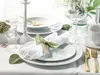 A beautifully set table with white porcelain plates, gold cutlery, and a white candlestick, suggesting an elegant dining experience. Produktbild-Vorschau