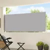 A grey retractable side awning is extended on a balcony, with outdoor furniture and plants visible. Voir les images du produit