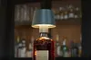 A close-up of a unique table lamp made from a liquor bottle, displayed in front of a blurred bar background with shelves of bottles. Produktbild-Vorschau