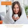A woman wrapped in a white blanket holding a mug. Produktbild-Vorschau