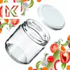 A glass jar and its lid are shown, surrounded by various fresh vegetables and herbs, suggesting preservation or cooking. Podgląd zdjęcia produktu