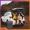 Two people sitting in the open trunk of a car with a suitcase next to it. Náhled obrázku produktu