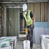A construction worker is mixing material in a bucket with a power mixer on a construction site. Podgląd zdjęcia produktu