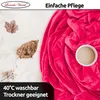 A pink fleece blanket is draped over a surface, with dried leaves and a small cup placed on it. Text overlays provide product information. Produktbild-Vorschau