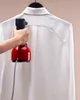 A hand is holding a red and black handheld steamer to a white shirt hanging on a hanger. Anteprima dell’immagine prodotto