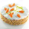 A close-up shot of a round cake decorated with marzipan carrots and green icing. Produktbild-Vorschau
