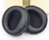 Two black ear pads for headphones are shown on a light-colored surface with a wooden stand in the background. Náhled obrázku produktu