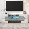 A modern TV stand with a large black television mounted above it, in a well-lit room with a striped rug on the floor. Podgląd zdjęcia produktu