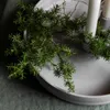 A close-up shot of a juniper branch draped over a light gray candle holder with white candles. Produktbild-Vorschau