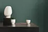 A minimalist arrangement of decorative objects on a dark wooden surface against a teal wall. Produktbild-Vorschau