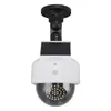 A white and black solar-powered security camera dummy with a dome lens and LED lights is shown against a white background. Produktbild-Vorschau