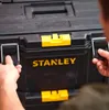Hands are shown operating the latches on a black Stanley tool box with yellow accents. Voir les images du produit