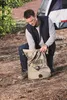 A man is kneeling on the ground, packing a bag next to a tent. Podgląd zdjęcia produktu