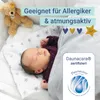 A newborn baby sleeping peacefully under a blanket, with a teddy bear nearby. The image includes marketing text and a certification logo. Produktbild-Vorschau