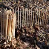 A wooden fence made of thin stakes, with a bundled section of stakes on the left, surrounded by fallen leaves. Produktbild-Vorschau