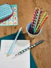 A collection of colorful pencils and a pencil case are arranged on a wooden surface, with a notebook open to practice writing exercises. Produktbild-Vorschau