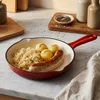 A red cast iron pan filled with sausage, sauerkraut, and dumplings sits on a marble countertop. Anteprima dell’immagine prodotto