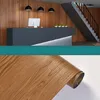 A collage showing a reception area with a desk and stairs, and a roll of wood-patterned adhesive vinyl. Anteprima dell’immagine prodotto
