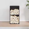 A black, two-tiered firewood rack filled with logs, placed against a light gray wall and on a wooden floor. Produktbild-Vorschau