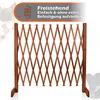 A wooden expandable pet gate is shown standing upright against a white background. The gate is made of wooden slats arranged in a diamond pattern. There are faint outlines of dogs in the background and a text overlay at the top. Produktbild-Vorschau