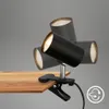 A black desk lamp with three adjustable spotlights is clamped to a wooden surface. Náhled obrázku produktu